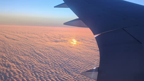 the wing of a jet above the orange cloud cover during sunrise