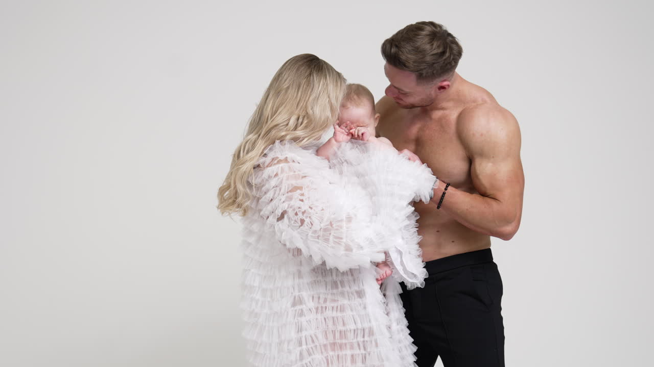 Caucasian parents with their little cute baby boy in studio. Mom and dad calming down their crying kid. White backdrop.