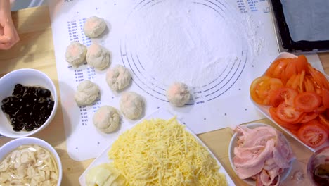 woman makes dough balls for pizza with different ingredients. hands close-up.