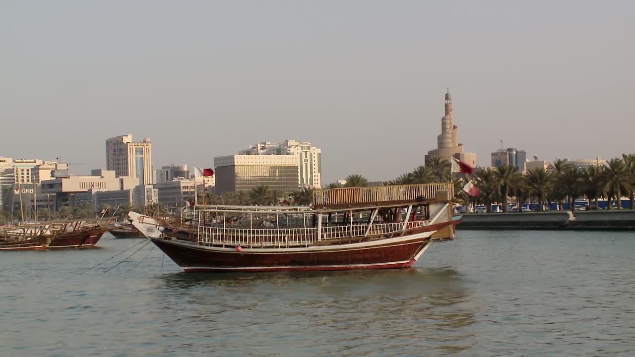 un dhow árabe anclado en el puerto interior de doha, qatar, con el icónico minarete y el moderno horizonte de doha a la vista