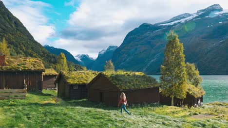 blonde girl with pink sweater and jeans running through a beautiful scenic grass field towards abandoned old houses next to large mountains anda beautiful ocean