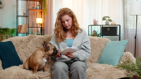 caucasian woman looking worried at bills on home sofa while pug dog senses stress and stays close