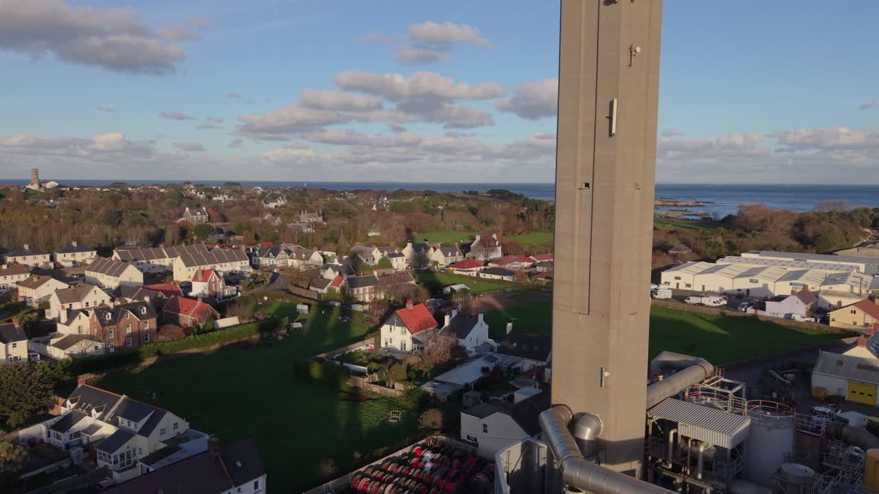 Filmato lento con drone di St Sampson, Guernsey, del complesso della centrale elettrica e della ciminiera che vola verso il porto di Bordeaux sotto il sole dorato con un cielo e un mare interessanti sullo sfondo.