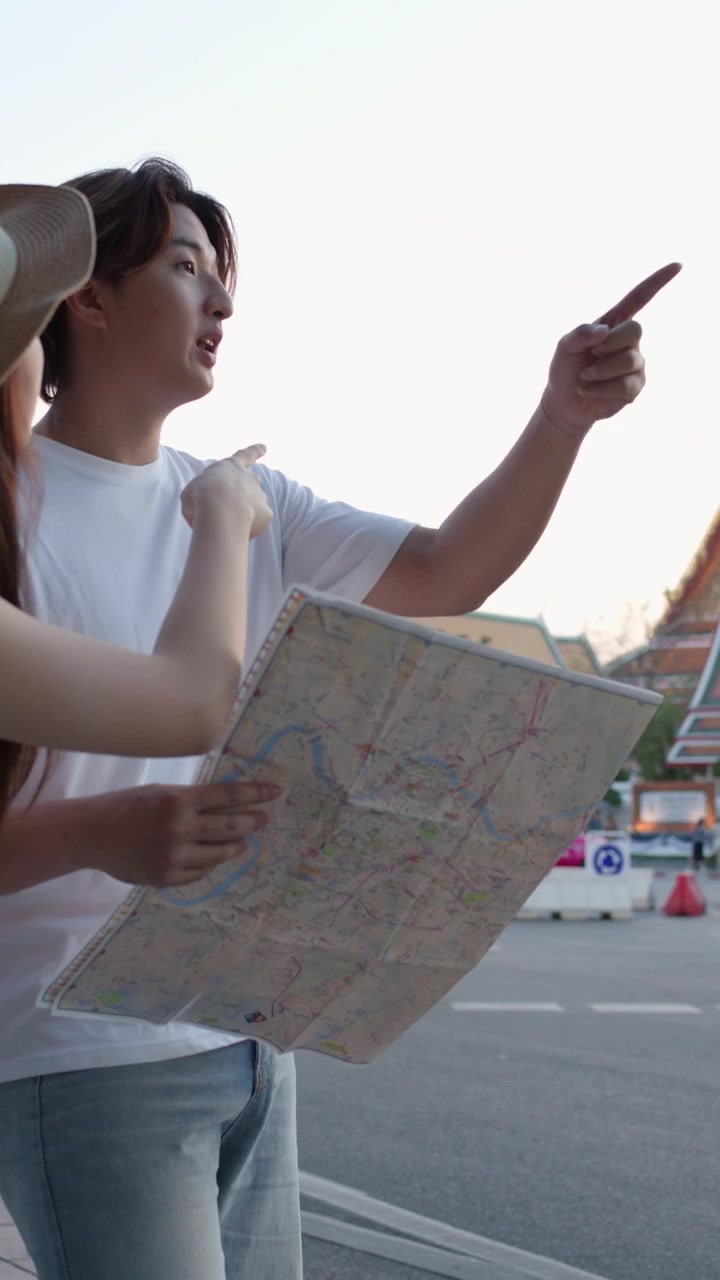 柔らかな夕暮れの光の中、街の通りで紙の地図を見ながらランドマークを指差す若い観光客