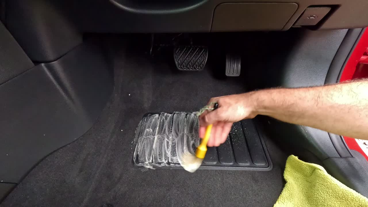 Cleaning footwell carpet plastic inside car with detailing brush and all purpose cleaner