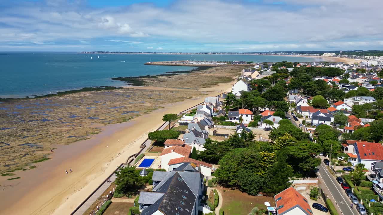 Bonne Source beach at low tide, oceanfront houses, sandy beach, and Pornichet marina in background, France. Aerial backward