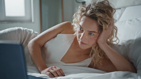 relaxed woman watching computer online. closeup serene girl lying on cozy bed