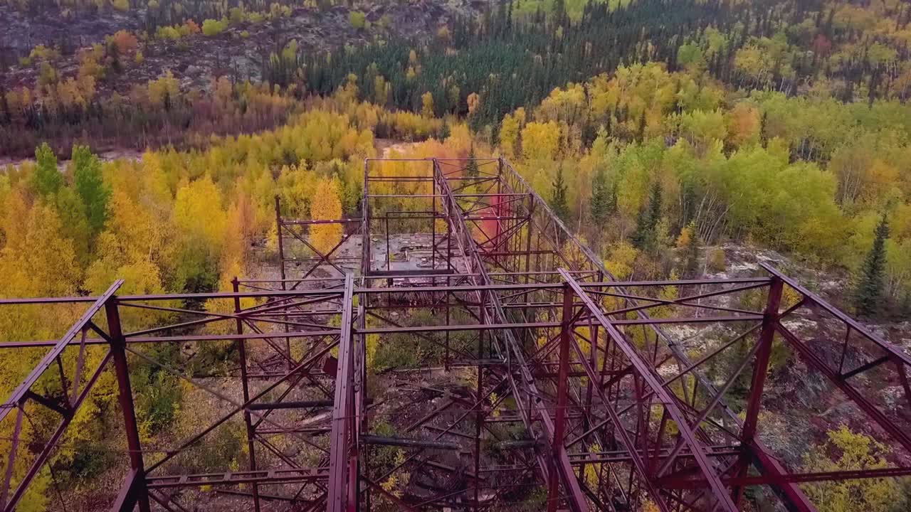 toma aérea de un marco de construcción de una mina abandonada en el bosque boreal en otoño con un lago en el fondo