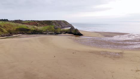 people walking across the vast sandy beach of three cliffs bay during low tide