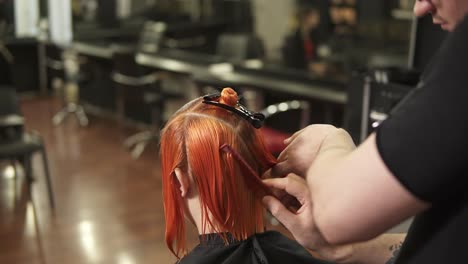 Young-woman-getting-her-hair-dressed-in-hair-salon.-Stylist-hairdresser-at-work.-Man-hairdresser-brushing-hair-in-beauty-salon