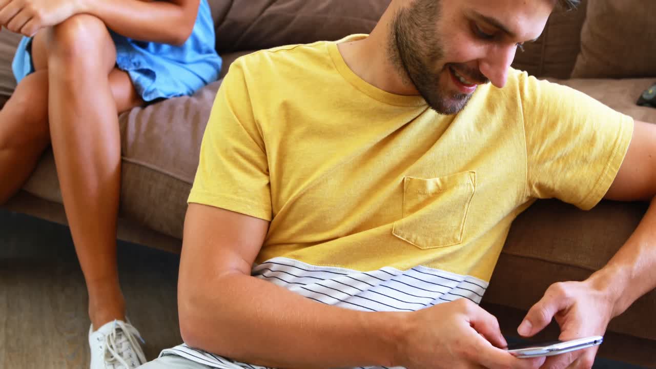 Uomo che scrive messaggi e donna che sbircia il suo cellulare da dietro