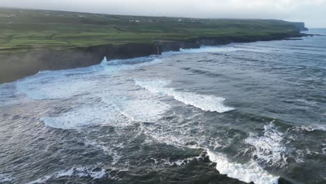 doolin's rugged coastline with waves crashing against cliffs, green fields in the distance, aerial view