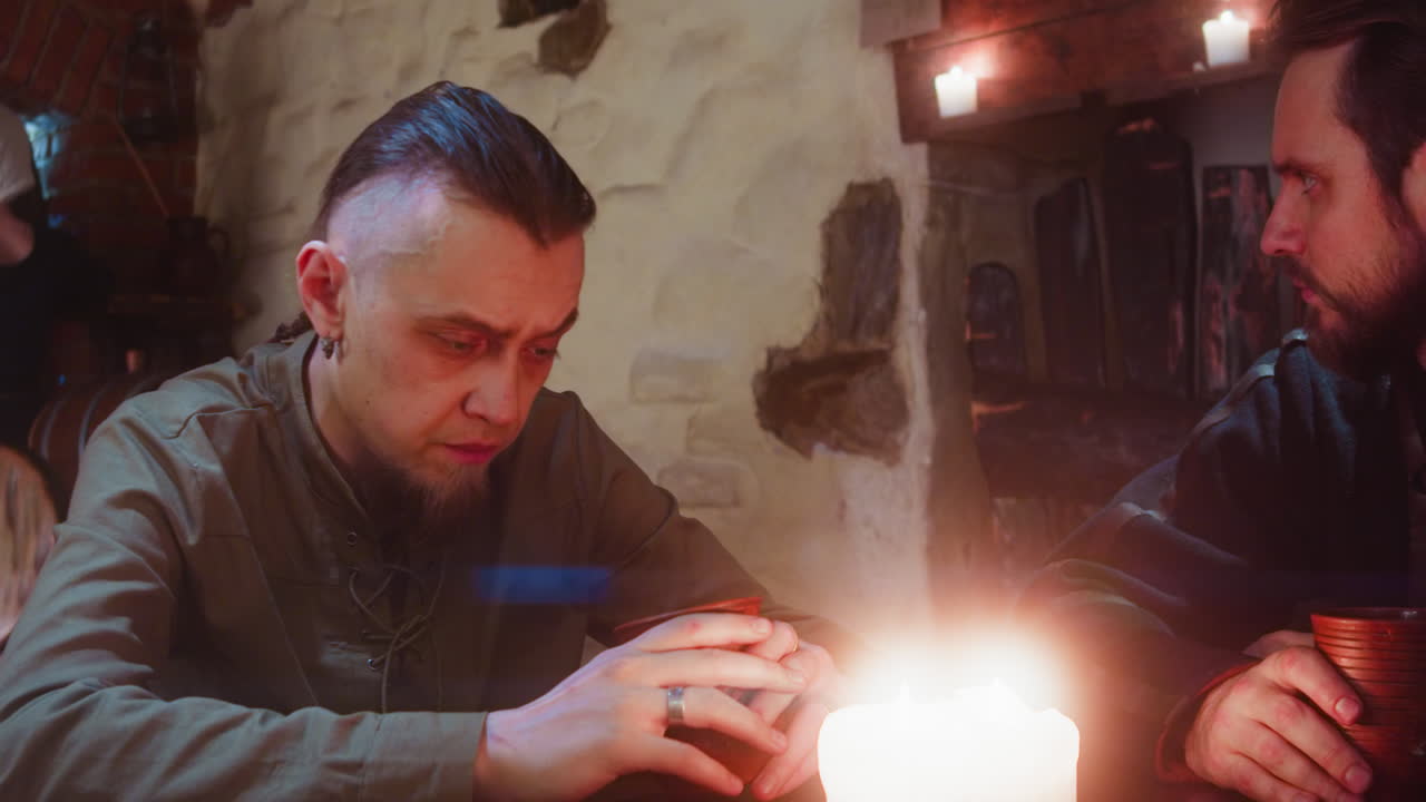 amigos frustrados beben alcohol en la taberna. un tipo barbudo molesto golpea la mesa con el puño hablando con un amigo en un pub medieval. campesinos pobres enojados en un bar de fantasía