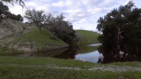 drone rises above short dam revealing a small pond