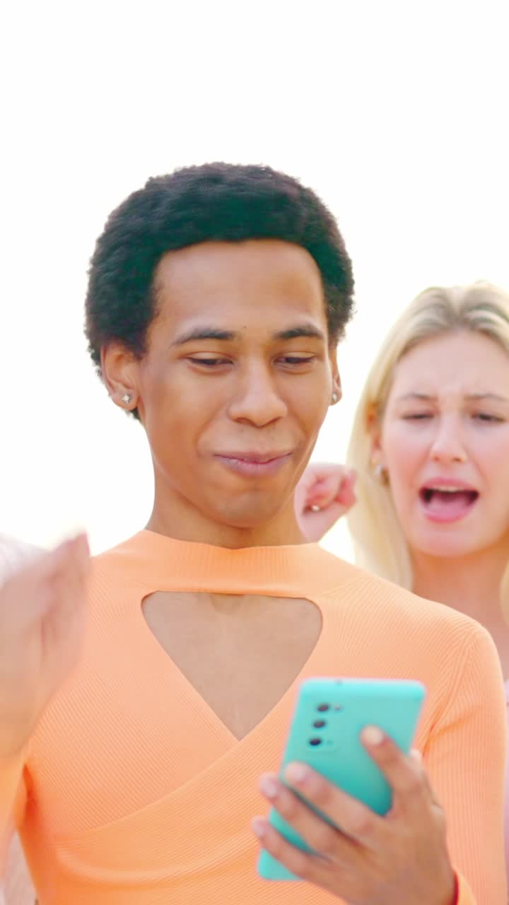 Multi-ethnic friends celebrating while using a mobile phone outdoors