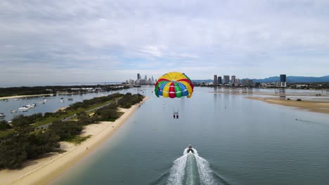 Farbenfrohes-Parasailing-Entlang-Eines-Beliebten-Ferienortes-An-Der-Küste-Mit-Einer-Städtischen-Skyline-Im-Hintergrund