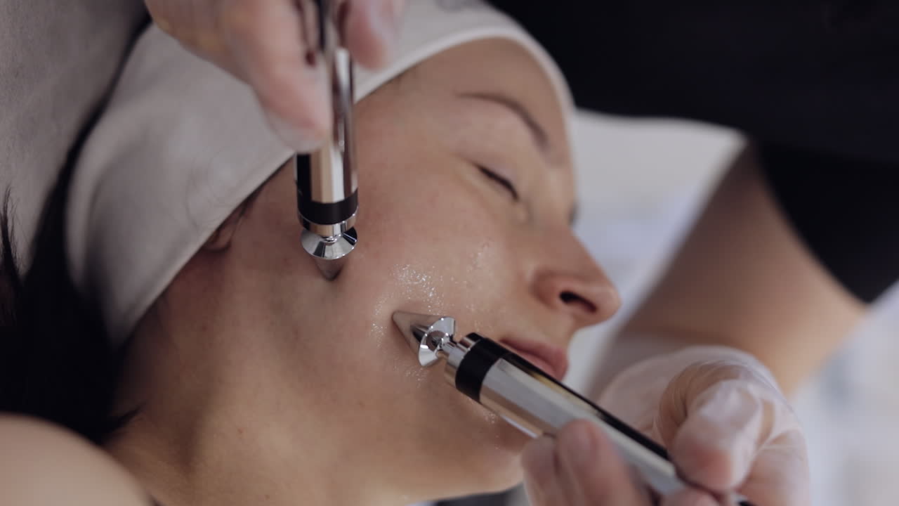 미용학자 의사는 스파 살롱에서 전기 충동을 사용하여 여성 마이크로 전류 얼굴 치료를합니다.