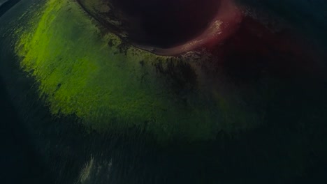 aerial drone flying over a green and red colored crater or a mountain range in iceland or greenland during a cloudy day. the crater has sharp edges and is circular in shape. moss and grass covering it
