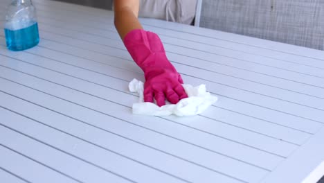 a person cleans a table using a spray bottle and cloth, wearing pink gloves. bright lighting enhances the clean environment