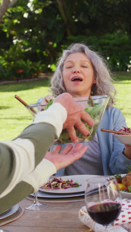 video vertical de una feliz familia caucásica cenando en el jardín