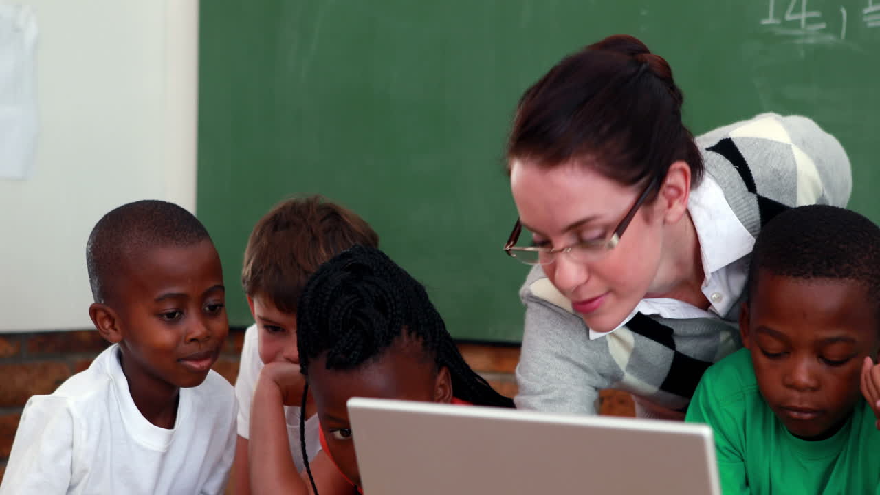 Pupils and teacher looking at laptop in classroom