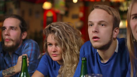 jóvenes con camisetas azules que están experimentando el momento decisivo del partido de los aficionados que luego se regocijan en la victoria de su equipo. los aficionados celebran la victoria en el bar de su equipo abrazo y la alegría de los fanáticos.