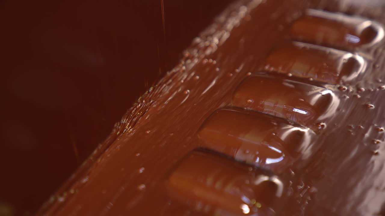 Thick layer of chocolate over the candies on the conveyor line. Sweets deepened into black chocolate. Manufacturing process of pigeon's milk candies close up.