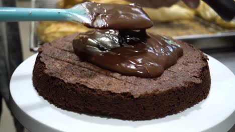 close-up shot of hand of chef spreading hot dark chocolate cream fudge all over rustic cake in bakery shop kitchen