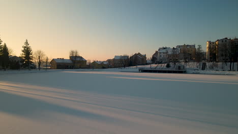 Aerial-flight-over-frozen-lake-covered-with-white-snow-during-sunset-in-nature