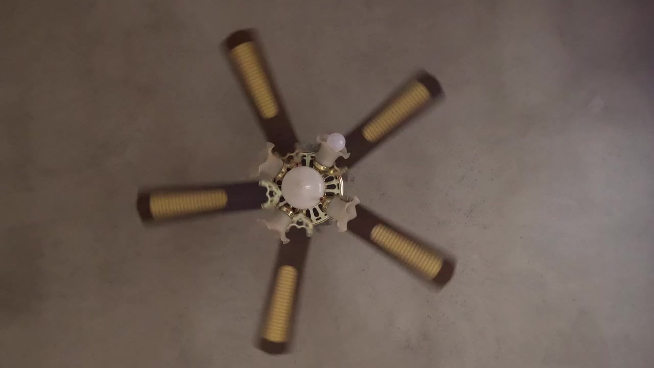 Ceiling fan rotating indoors with multiple blades and integrated lights, providing airflow and cooling. Household appliance improving air circulation and comfort in residential living space.