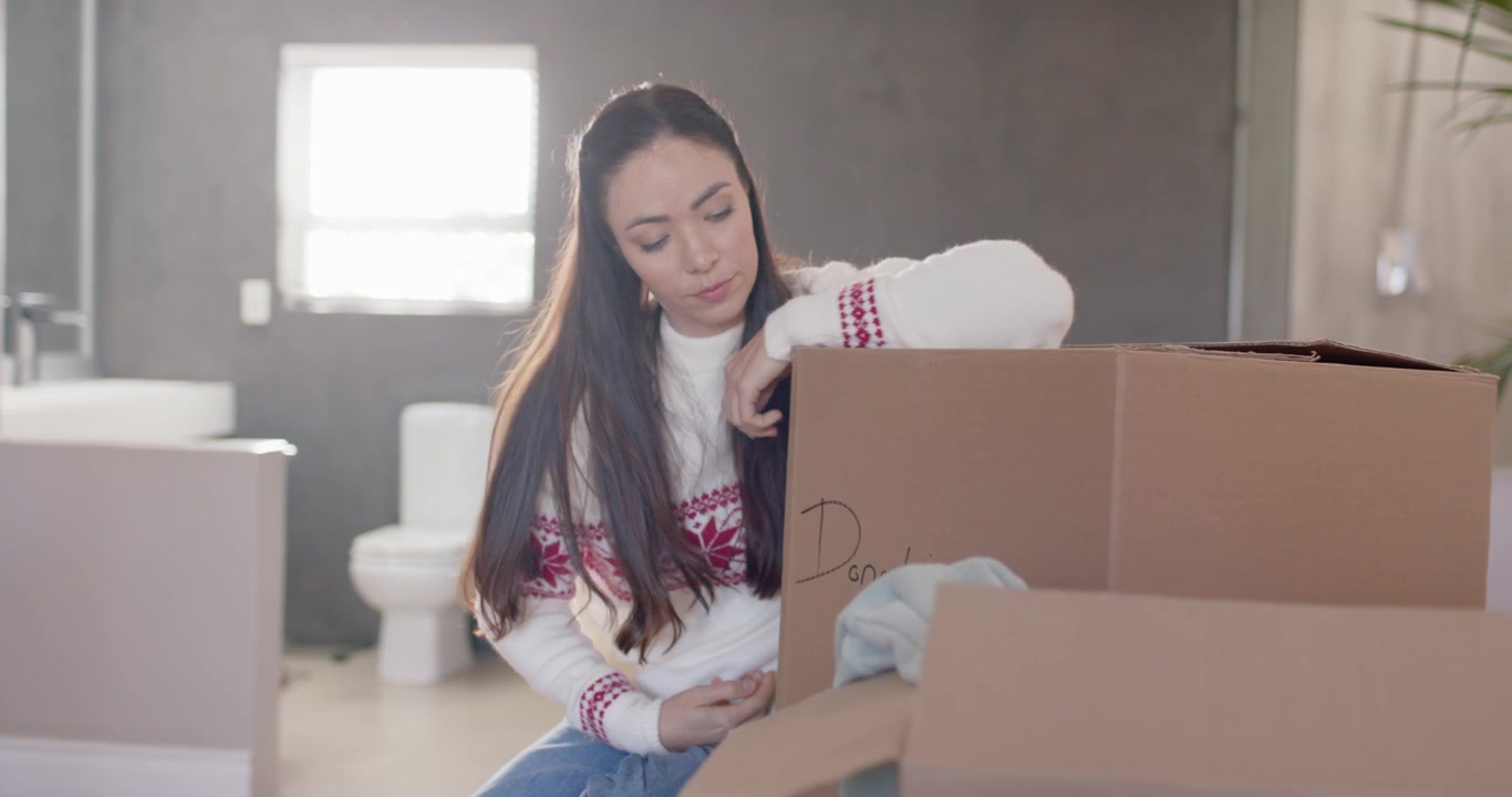 Donna con un maglione nordico rosso e bianco lavorato a maglia che solleva il coperchio di una scatola per donazioni a casa, smistando vestiti natalizi