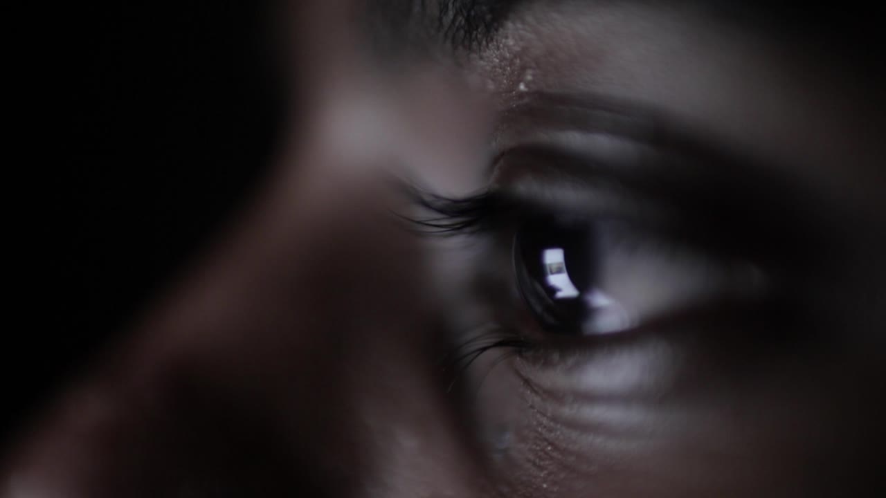 Eye of a dark skined girl scrolling through her phone in the dark close-up