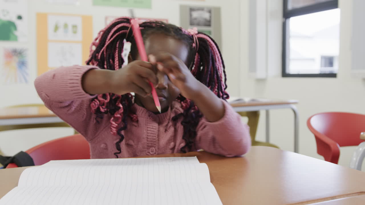 In classroom, African American girl holding pencil, ready to write in notebook, at school