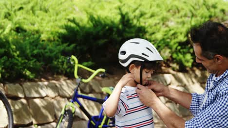 Father-assisting-son-in-wearing-bicycle-helmet-in-park