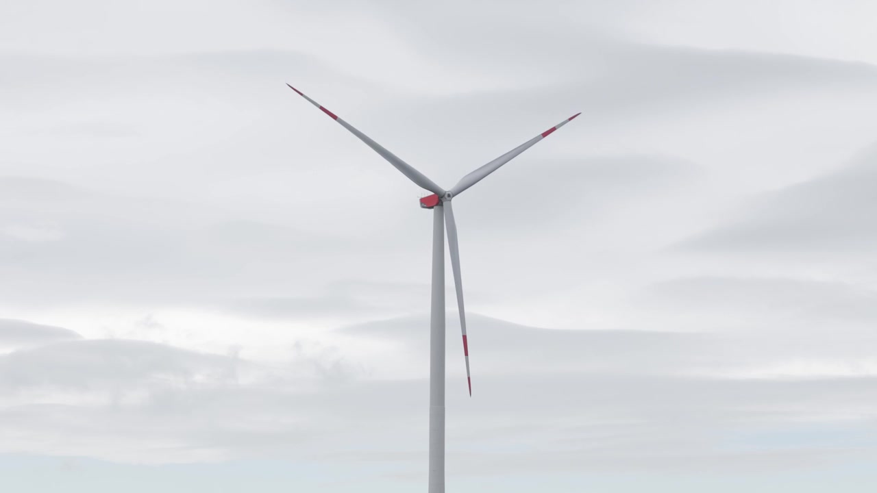 Turbina eolica che gira sotto cieli coperti con illuminazione soffusa e uno sfondo minimalista.