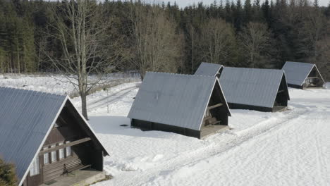 Toma-Aérea-De-Cabañas-De-Esquí-De-Madera-En-Un-Campamento-De-Esquí-De-Invierno,-Alojamiento-Alpino-En-Un-Hermoso-Paisaje-Cubierto-De-Nieve