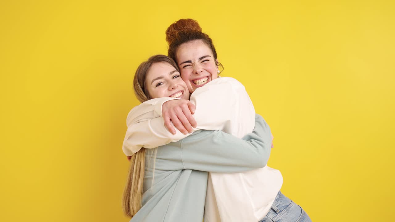 Two happy friends hugging each other on yellow background