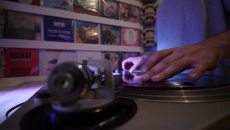 la parte inferior del cuerpo de dj se acerca cuando comienza a mezclar vinilos en el tocadiscos mientras las luces de colores parpadean en la lente ultra ancha