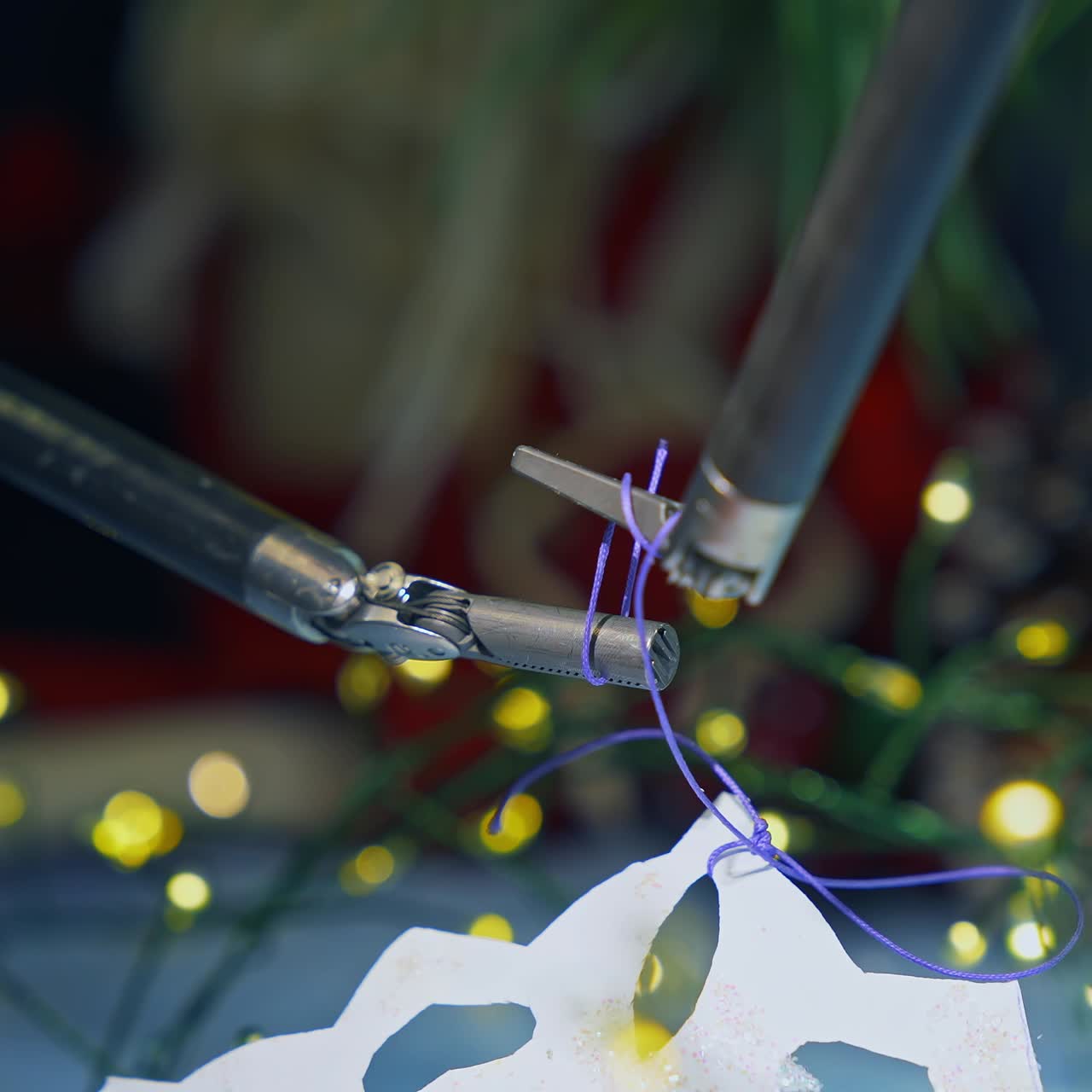 Tiny forceps of Da Vinci system tying a knot on a thread. Fastening the thread on the paper snowflake by robotic arms of Da Vinci surgical system. Close up