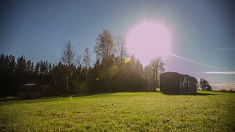 Timelapse-of-a-sunset-and-stars-becoming-visible-in-the-clear-sky-above-a-field-with-a-sauna-and-camping-wagon