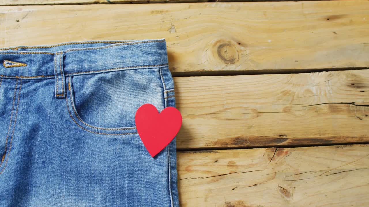 Primo piano di jeans con un cuore rosso su sfondo di legno con spazio per il testo.