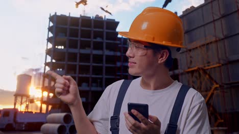 asian man worker using smartphone and pointing to side at construction site