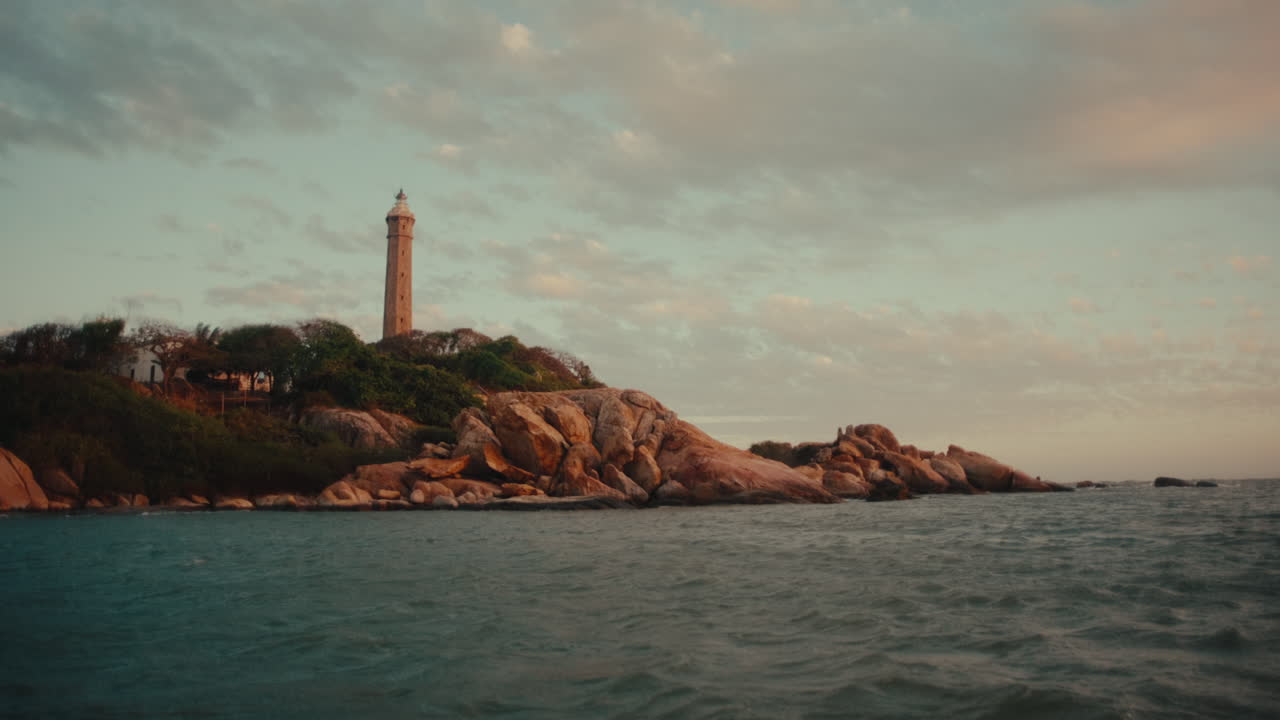 Faro che si erge su una costa rocciosa di un'isola, circondato dall'oceano sotto un cielo serale tenue.