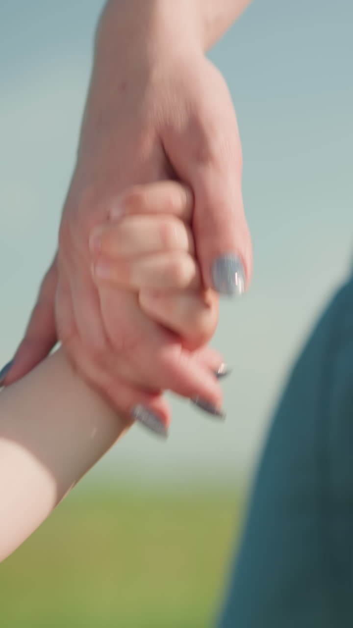 잔디을 가로질러 걸어가는 어린 소년의 부드러운 순간의 클로즈업, 부분적으로 보이는, 웃는, 그는 그의 어머니의 손을 잡고, 파란 드레스를 입고, 그녀의 얼굴을 보이지 않습니다.