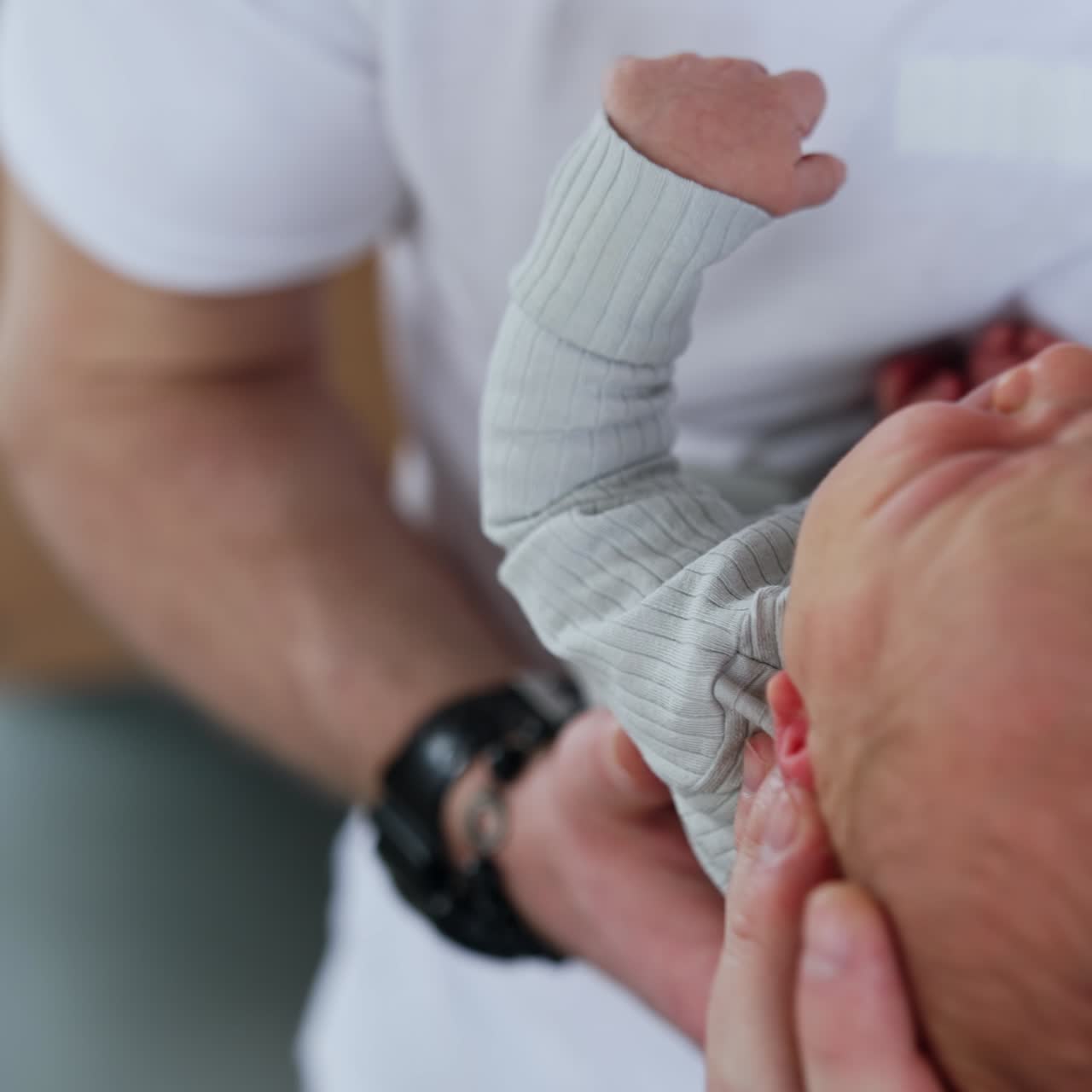 Male hands holding a cute tiny newborn. Infant boy starts to cry and wave little hands. Close up