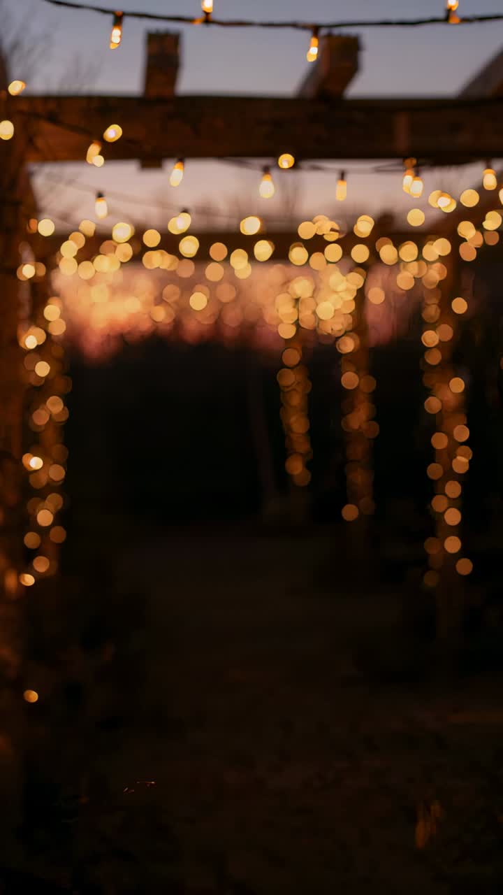 Vertical video: Panning camera revealing wooden pergola with lit string lights at dusk for ambience