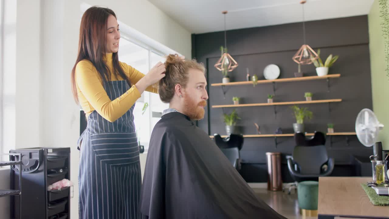 Caucasian female hairdresser untying long hair of male client at hair salon, in slow motion