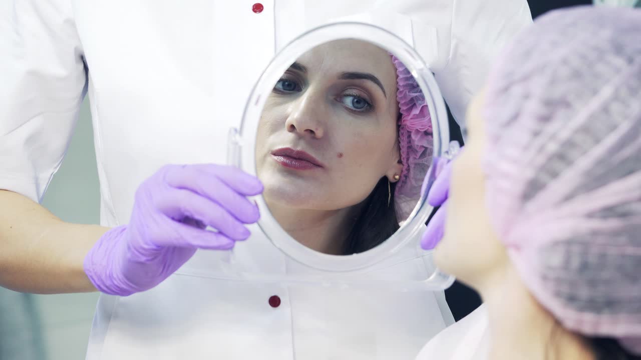 Patient looking at herself in the mirror after the lip augmentation procedure. Happy woman looks at her lips into mirror