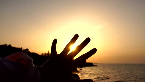 girl play with the rising sun at the sea at dawn time. handling sun rays between fingers.