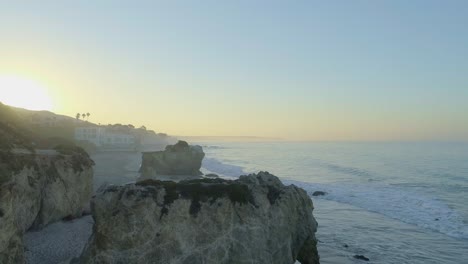 Aerial-shots-of-El-Matador-beach-over-breaking-waves-and-rocks-on-a-hazy-summer-morning-in-Malibu,-California